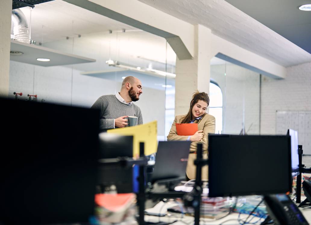 Two colleagues chatting and smiling in an office environment.