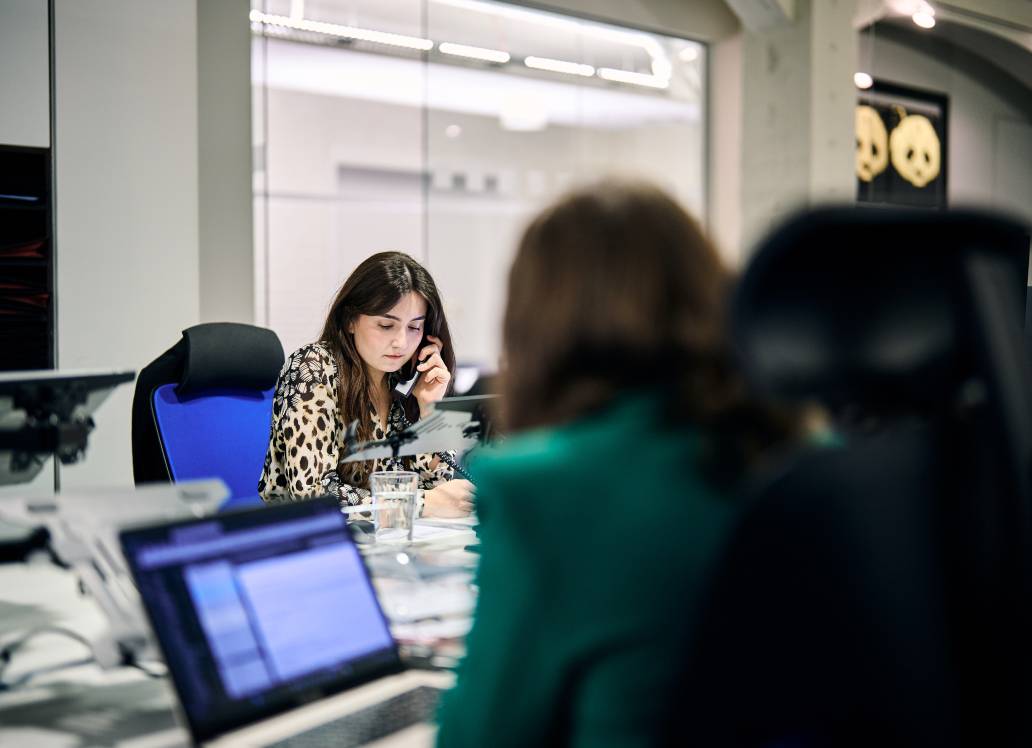Woman on the phone at a office desk, with a colleague in the foreground.