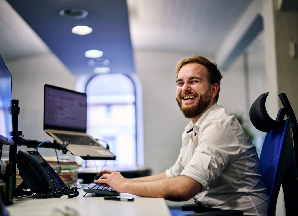 Man smiling at his desk in an office environment.